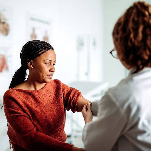A woman in a red sweater has her blood pressure checked by a female doctor.