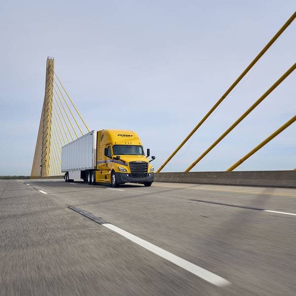 A yellow and white Penske semi-truck drives across a bridge.