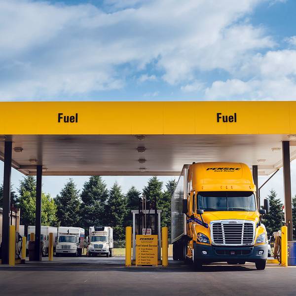 A yellow Penske semi-truck pulled up at a fuel station with yellow Fuel banner overtop.