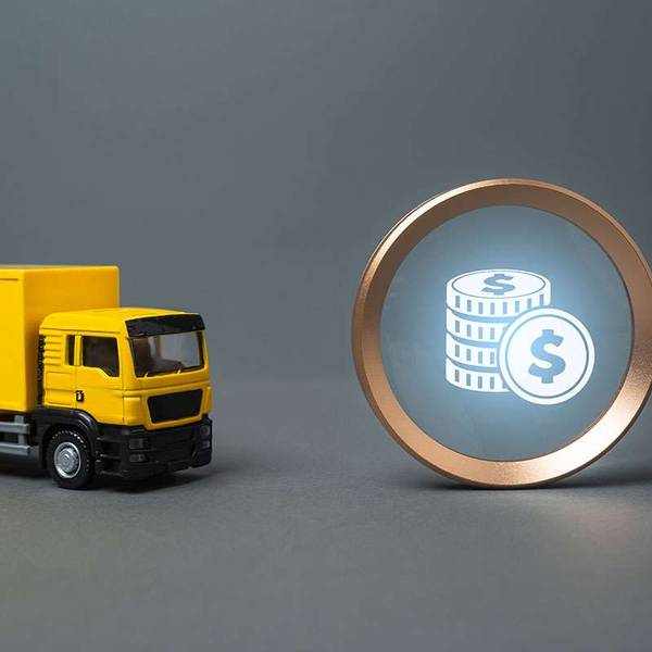 A yellow toy cabover truck sits next to a magnifying glass with a money icon inside.