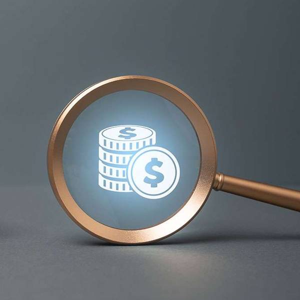 A yellow toy cabover truck sits next to a magnifying glass with a money icon inside.