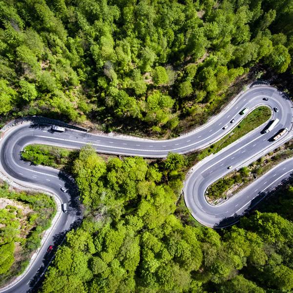 An aerial shot of trucks driving on a curvy road with lots of green trees.