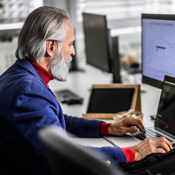An older man sits at a desk in front of three computer screens.