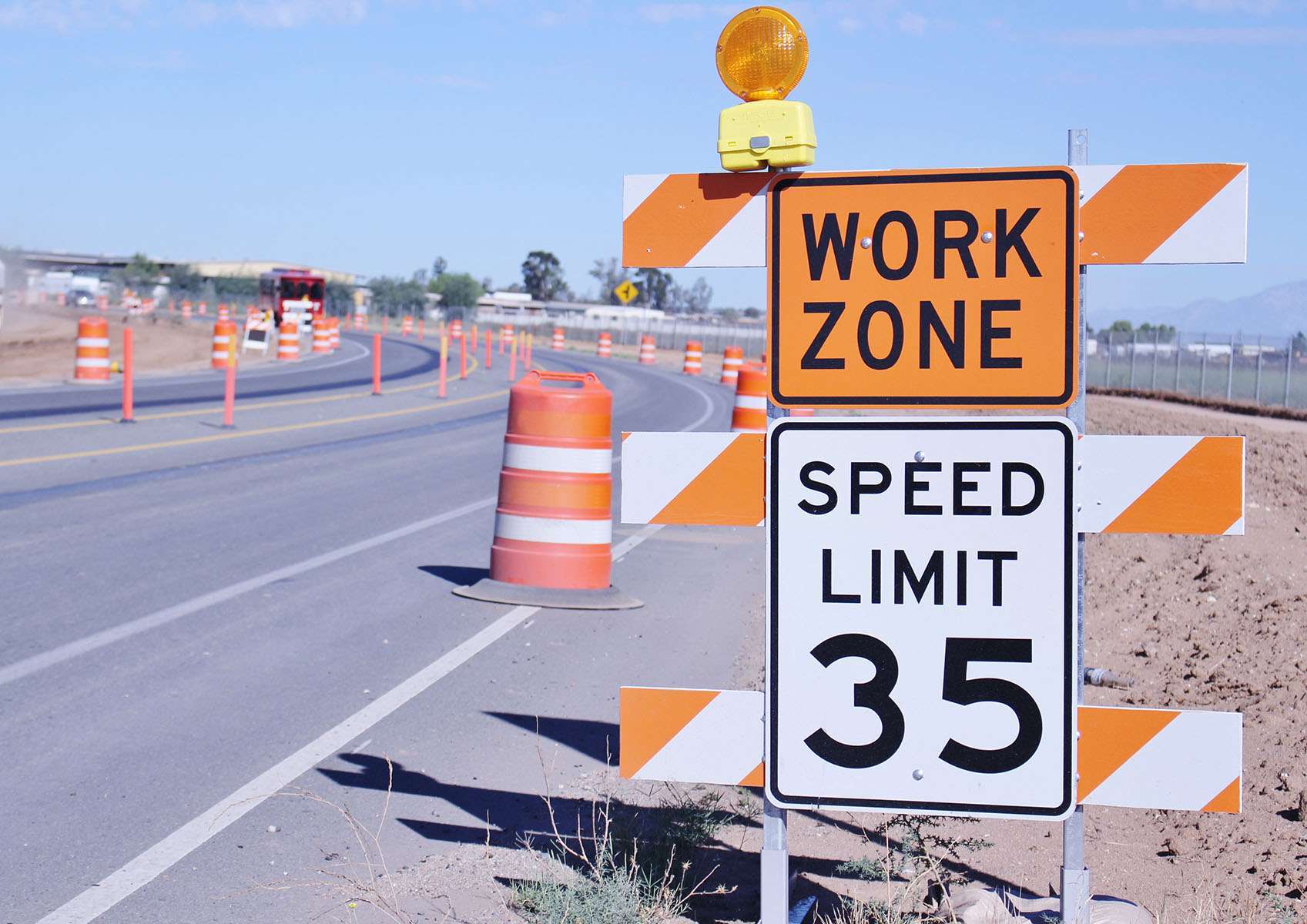 An orange work zone sign and speed limit 35 sign next to a road filled with orange construction barrels.