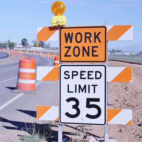 An orange work zone sign and speed limit 35 sign next to a road filled with orange construction barrels.