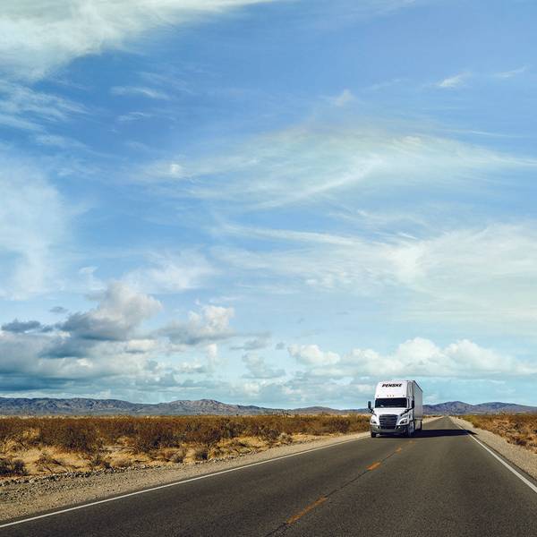 Blue cloudy sky, desert landscape with a white Penske semi-truck driving on a road.