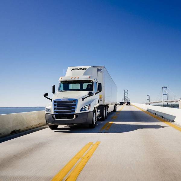 Blue sky with a white Penske semi-truck driving on a highway bridge.