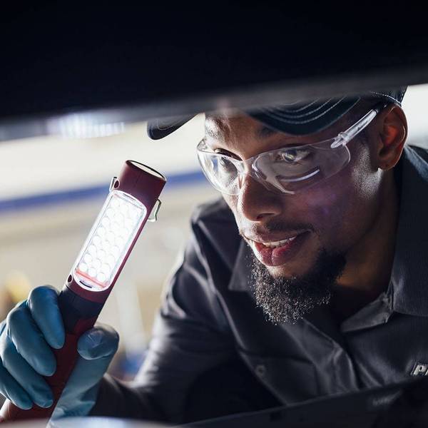 Closeup of a maitenance technician holding a flashlight looking under a truck.