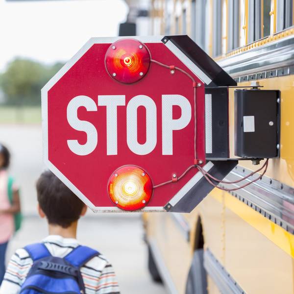 Closeup of the pop-out stop sign on the side of a school bus with kids walking by.