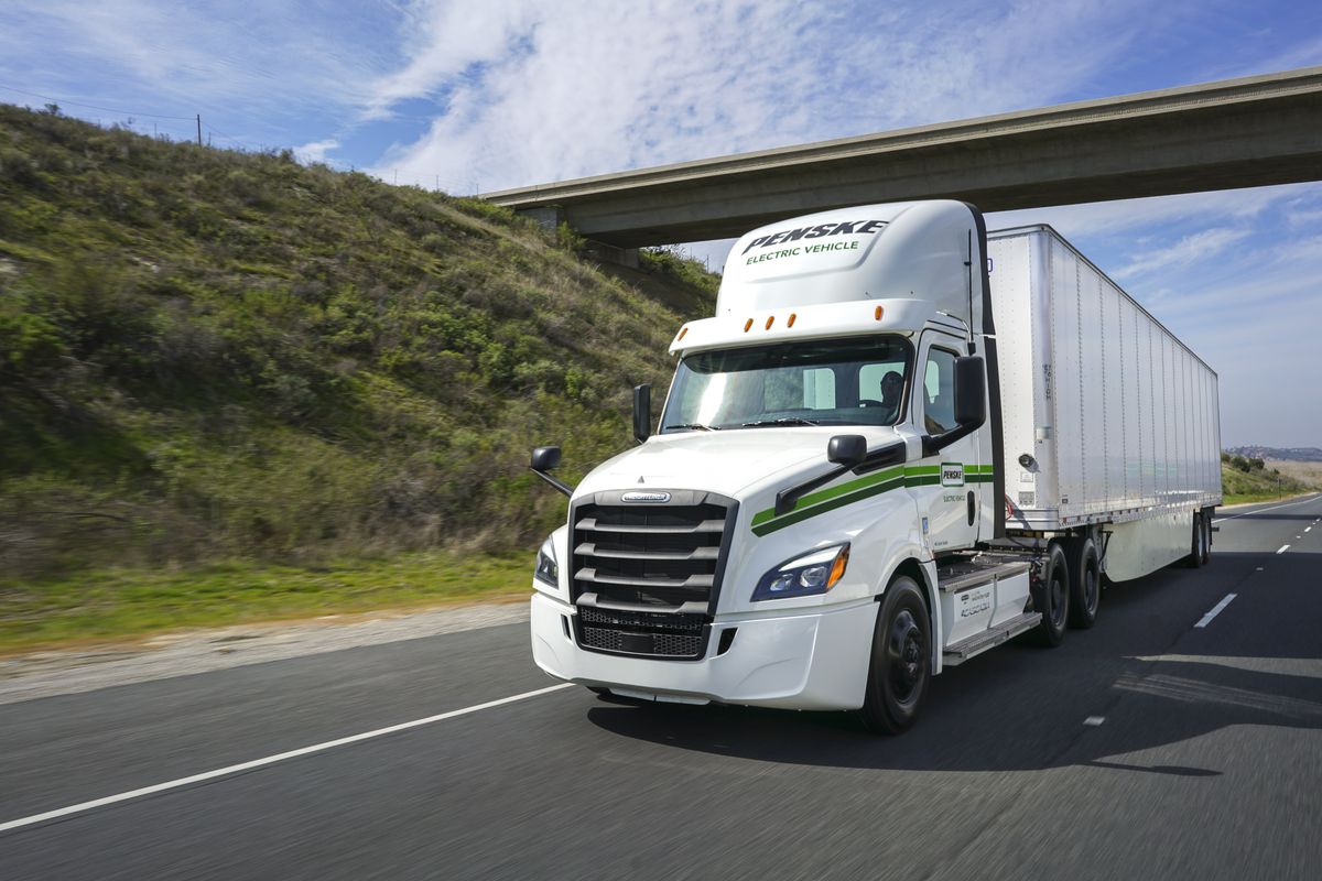 Electric tractor-trailer driving under a bridge.