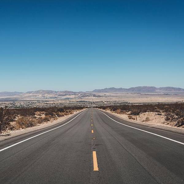 Long desert highway stretching towards distant mountains under a clear blue sky.