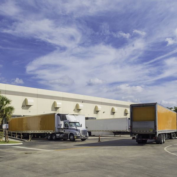 Multiple trucks maneuver around a warehouse yard.