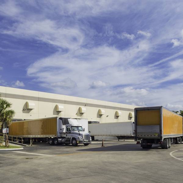 Multiple trucks maneuver around a warehouse yard.