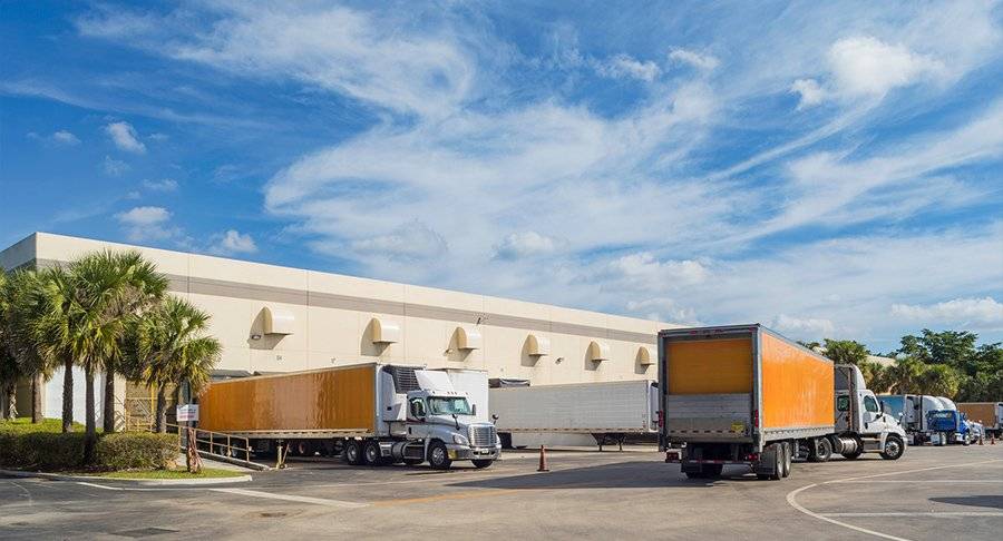 Multiple trucks maneuver around a warehouse yard.