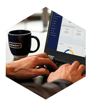 Person typing on a laptop in a cafe with a Penske mug