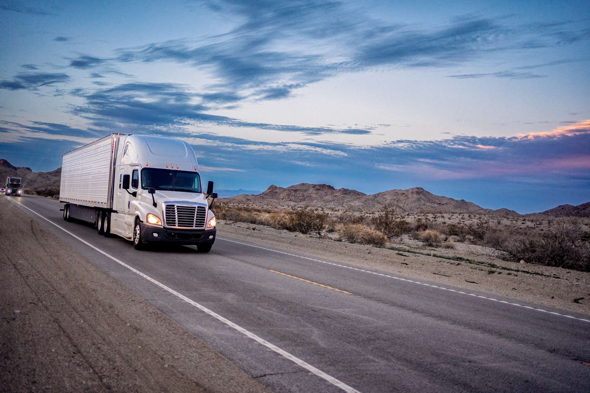 Semi trucks drive down a desert road.
