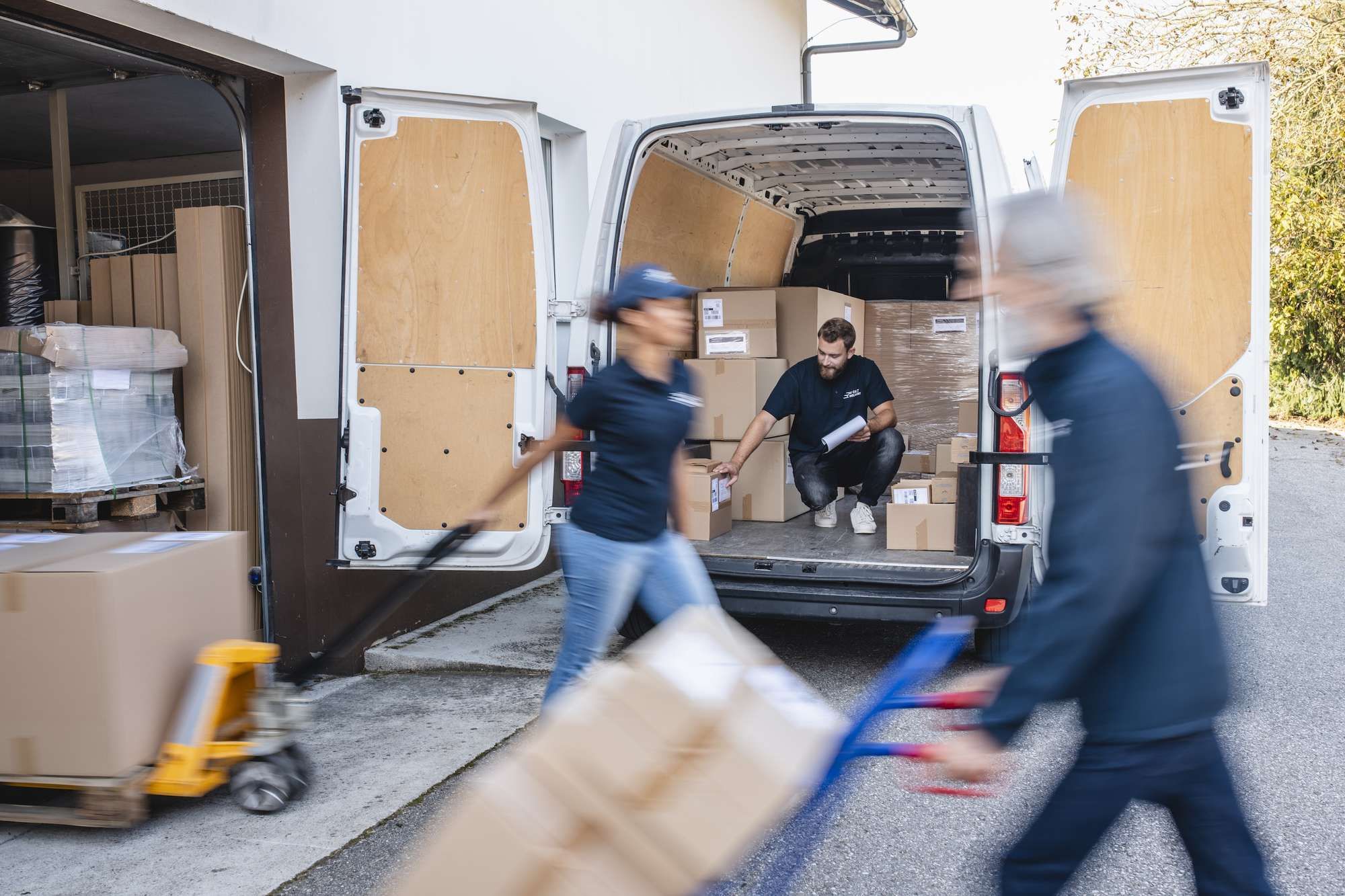 Three people load packages on and off a white cargo van.