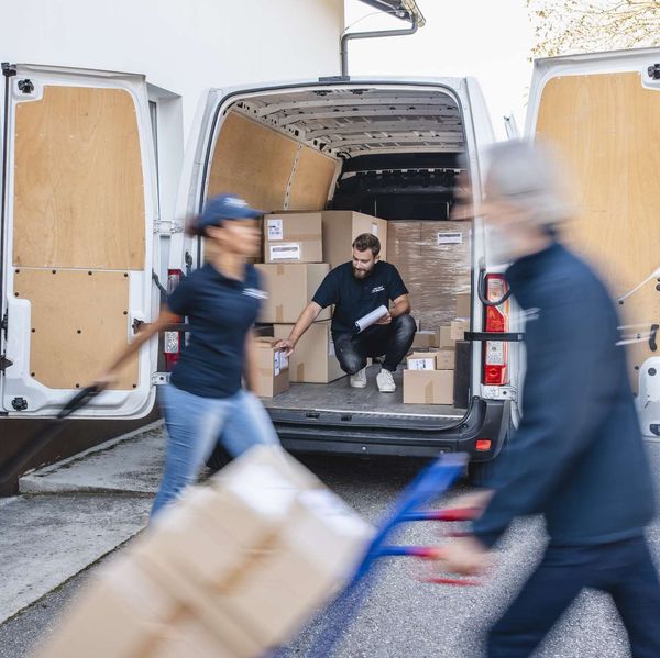 Three people load packages on and off a white cargo van.