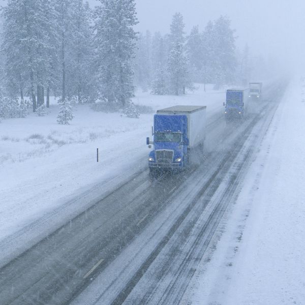Three semi-trucks drive up a snowy road on a winter day.