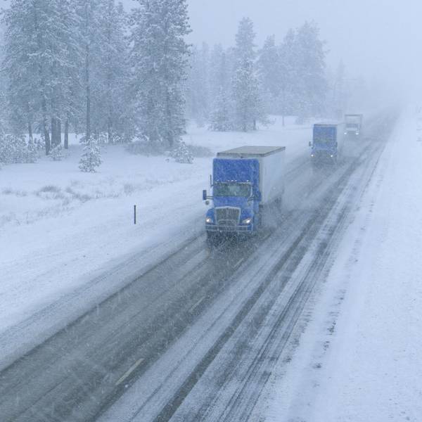 Three semi-trucks drive up a snowy road on a winter day.