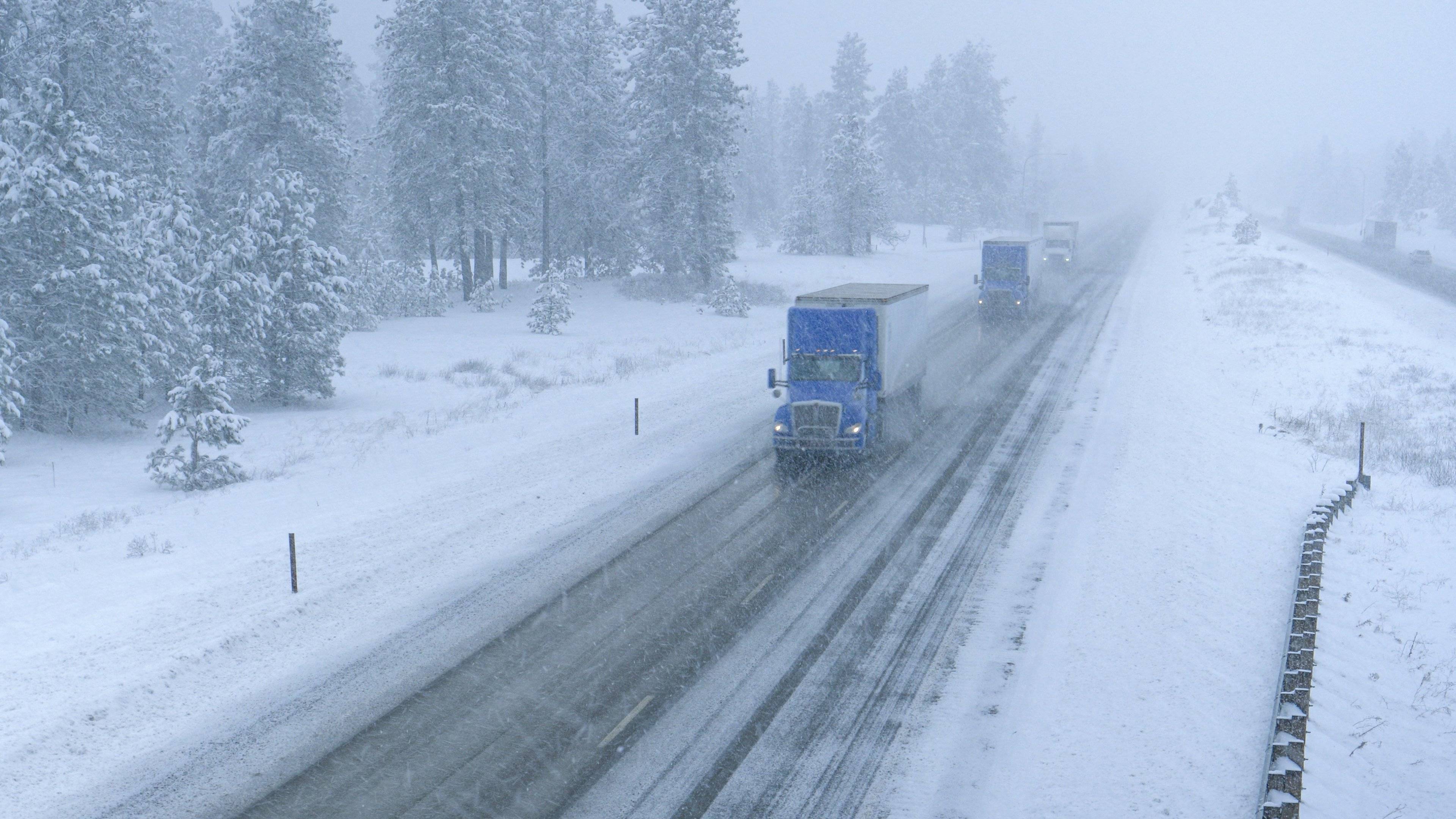 Three semi-trucks drive up a snowy road on a winter day.