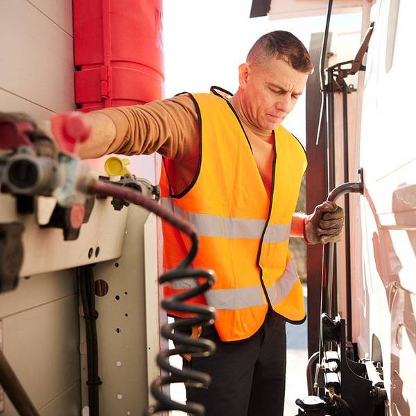 Truck driver in an orange vest and gloves examining semi-truck trailer brake coil for safety