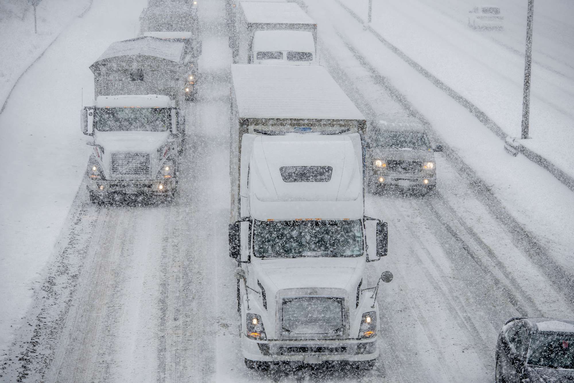Trucks and cars drive on very snowy roads while it snows.