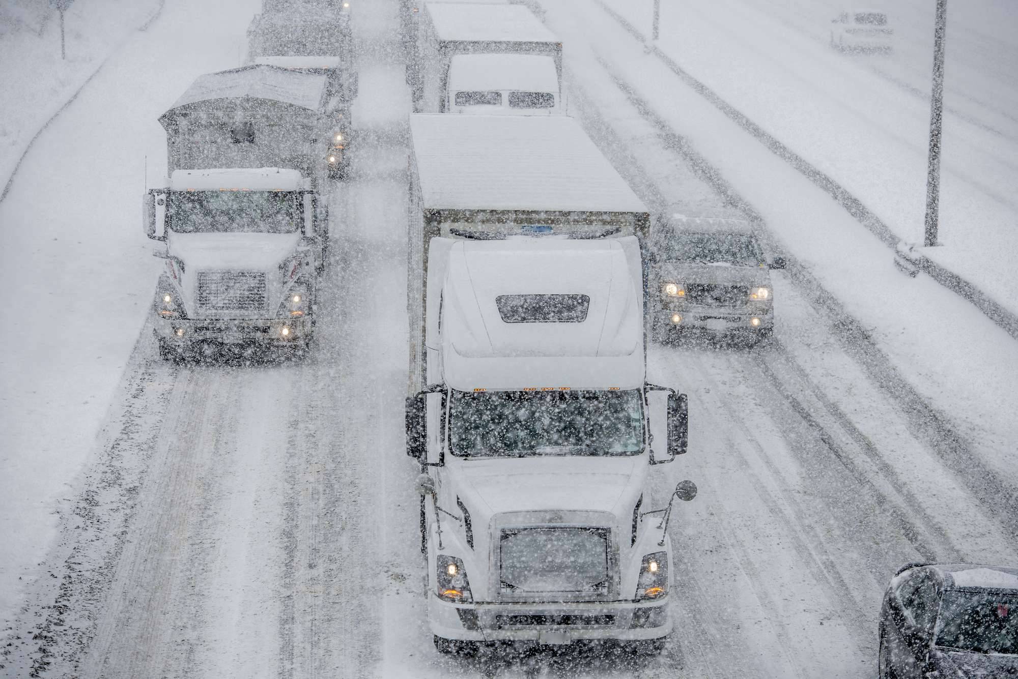 Trucks and cars drive on very snowy roads while it snows.