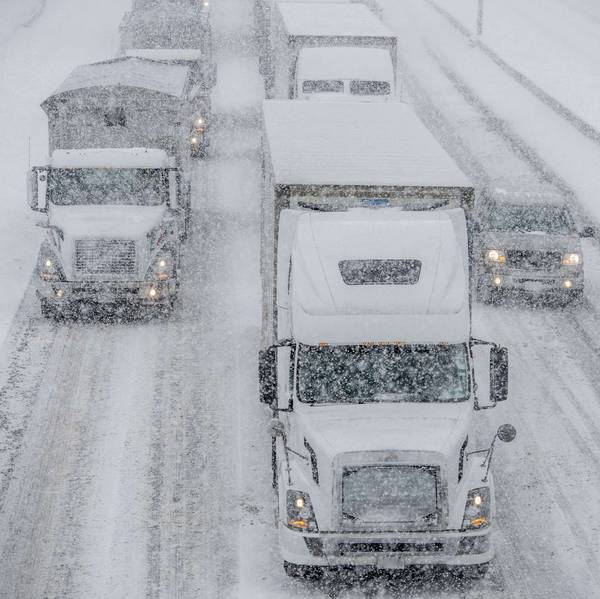 Trucks and cars drive on very snowy roads while it snows.