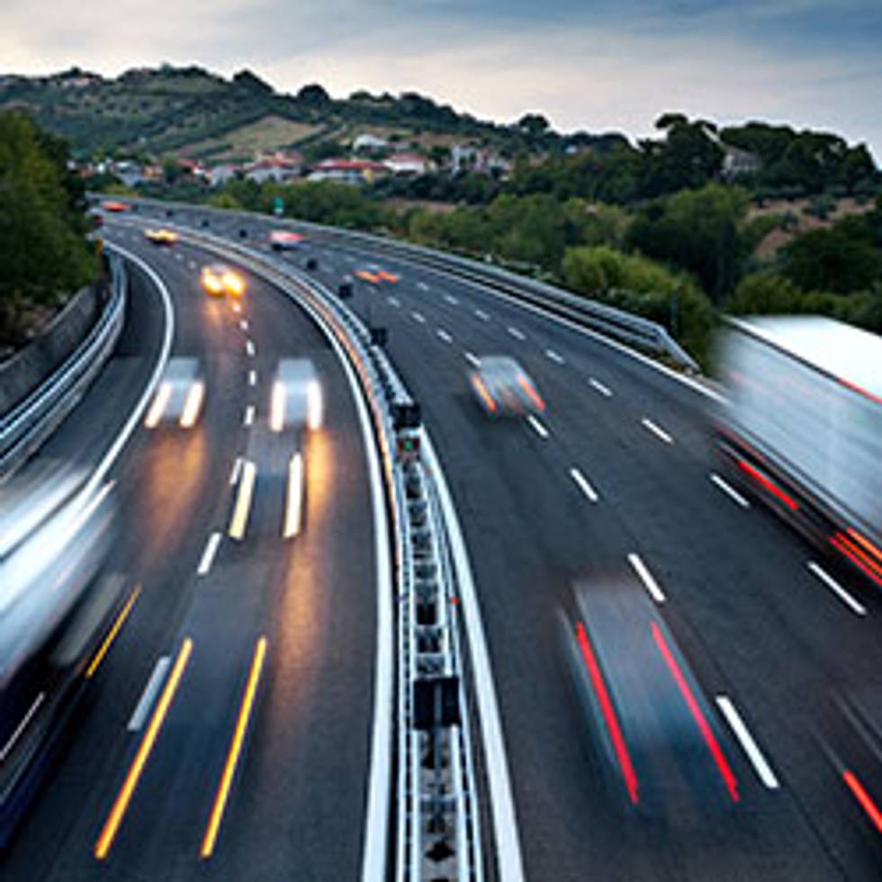 Trucks and cars drive up and down a freeway at night.