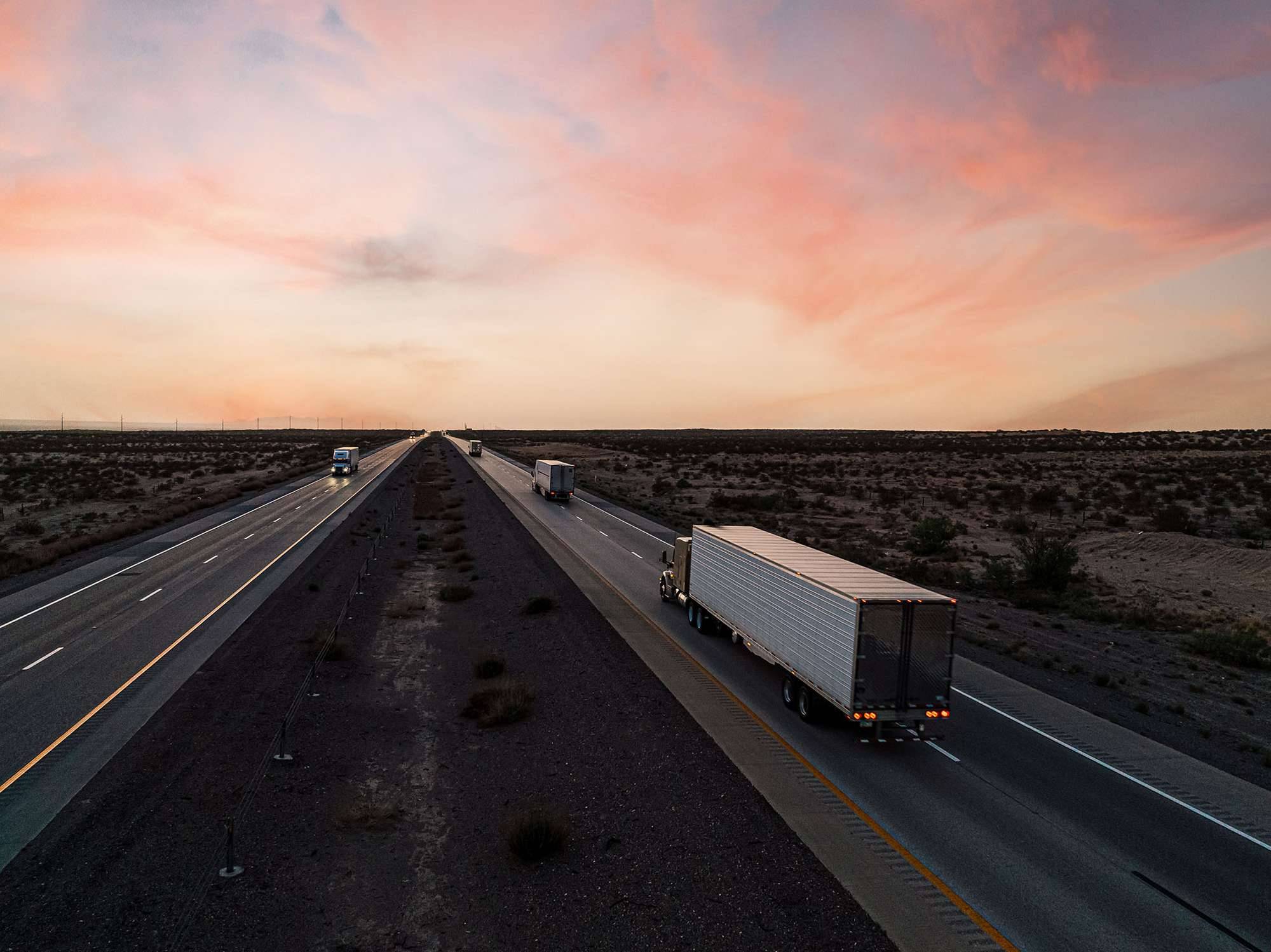 Trucks driving in opposite directions on a freeway at sunset.