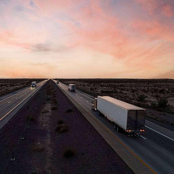 Trucks driving in opposite directions on a freeway at sunset.