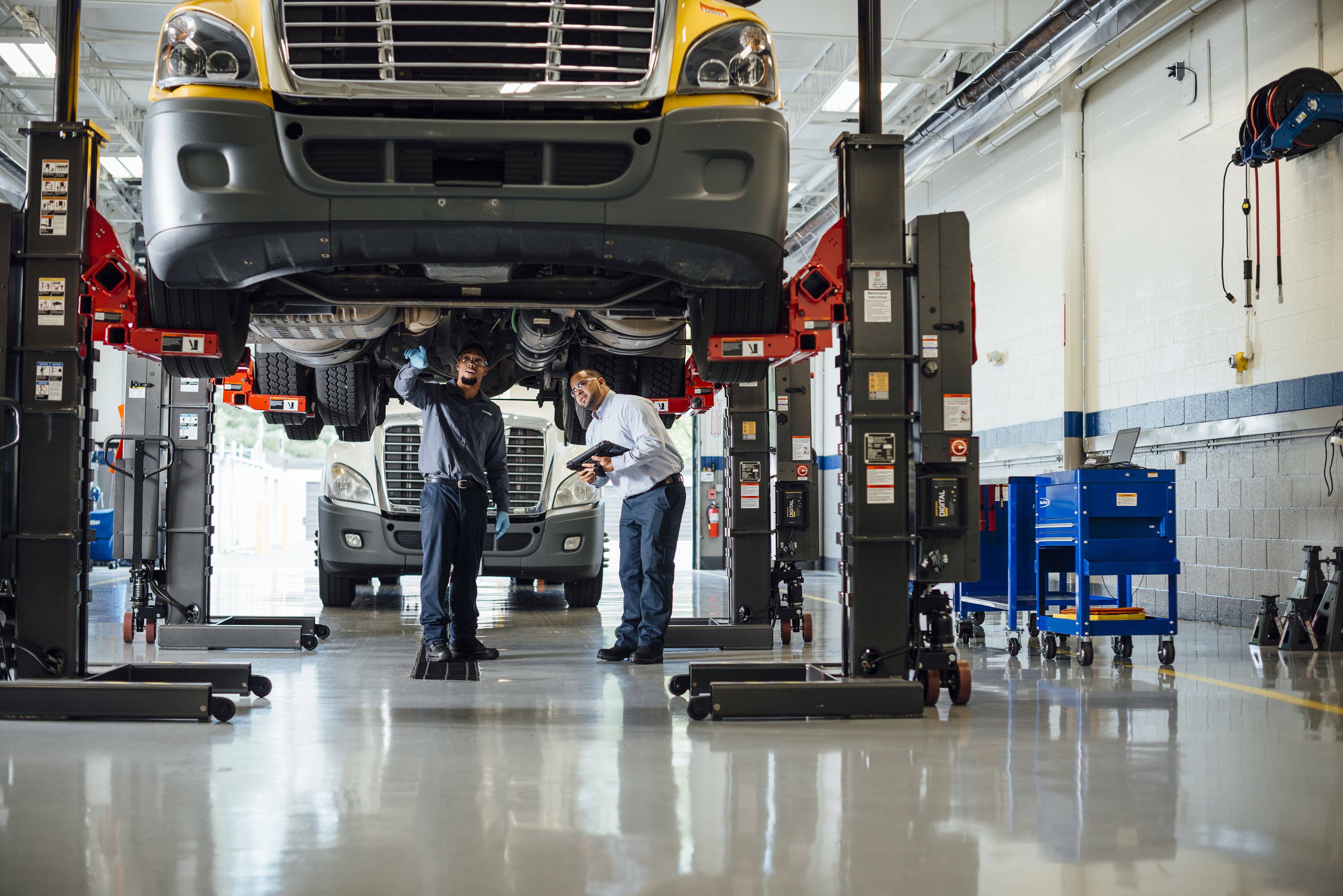 Two maintenance techs study the underside of a truck that's up on a lift.
