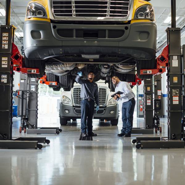 Two maintenance techs study the underside of a truck that's up on a lift.