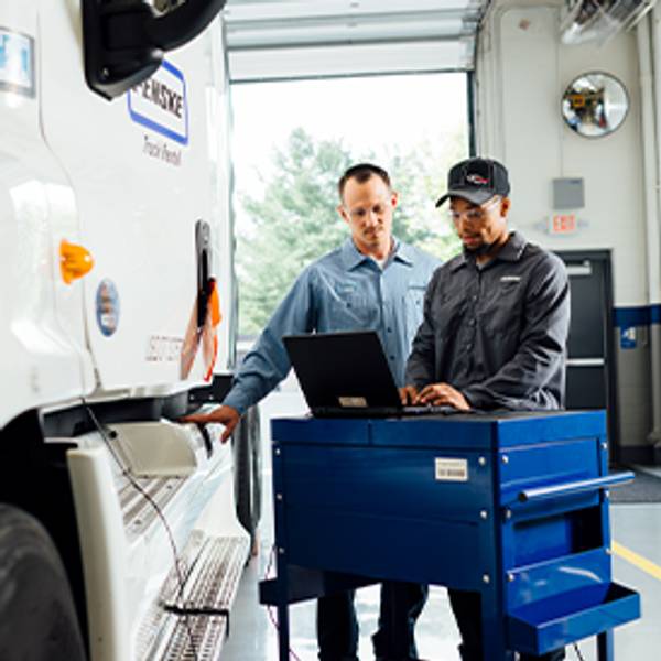 Two mechanics using a laptop beside a truck in a garage.