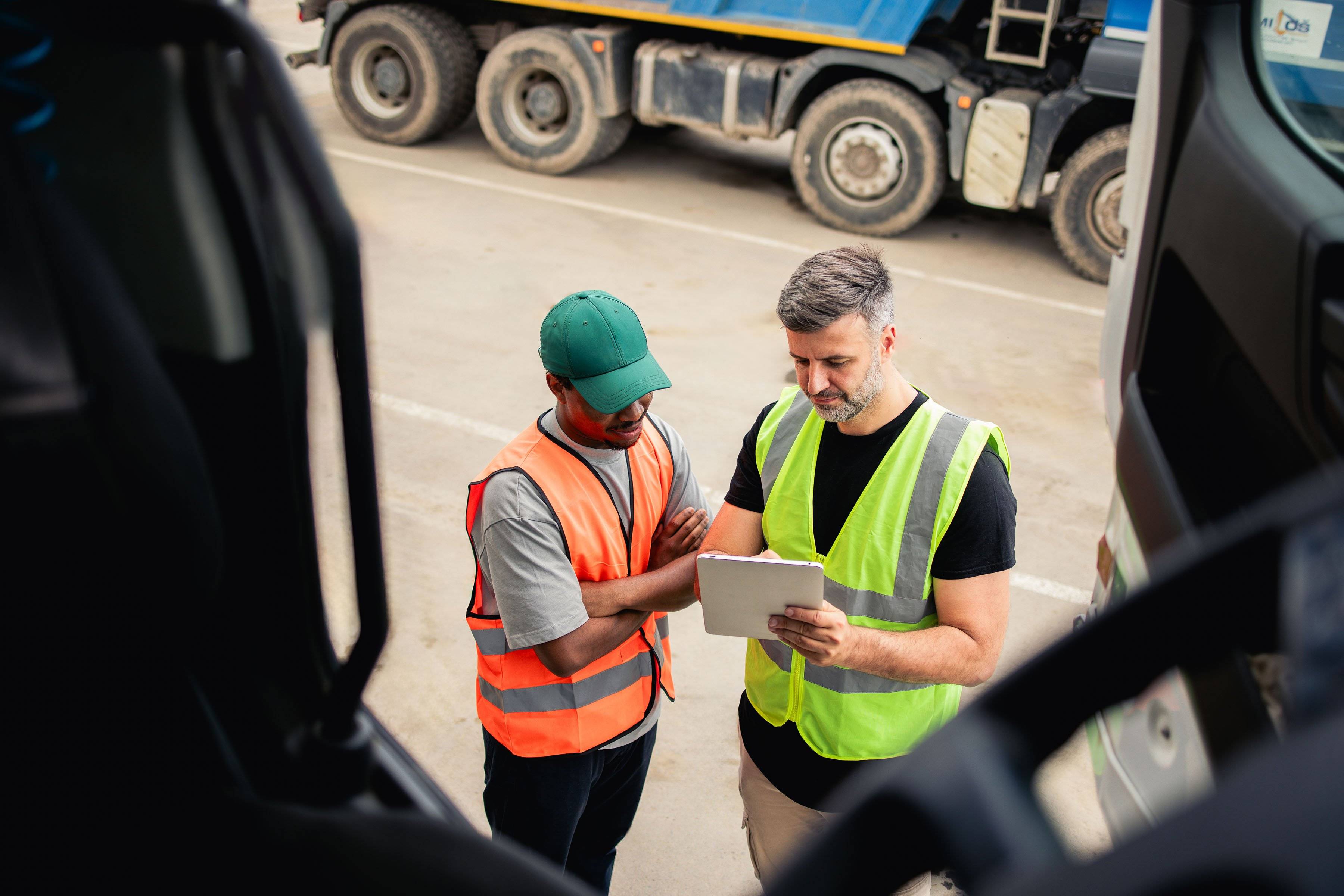 Two men stand outside a semi-truck cab looking at an ipad.
