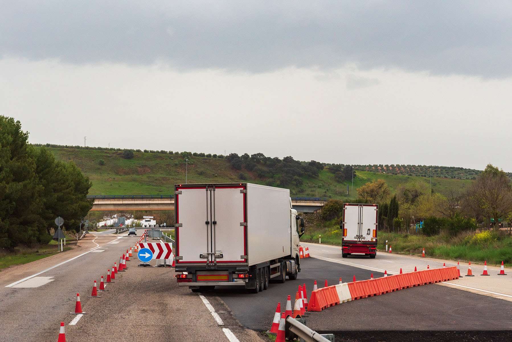 Two refrigerated semi-trucks maneuver lane changes in a construction zone.