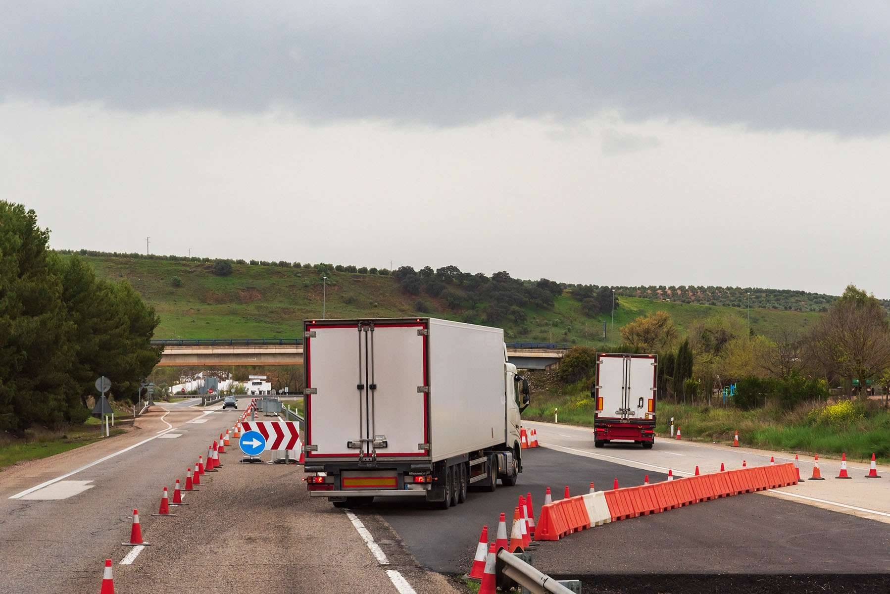 Two semi-trucks travel through a construction zone on a freeway.