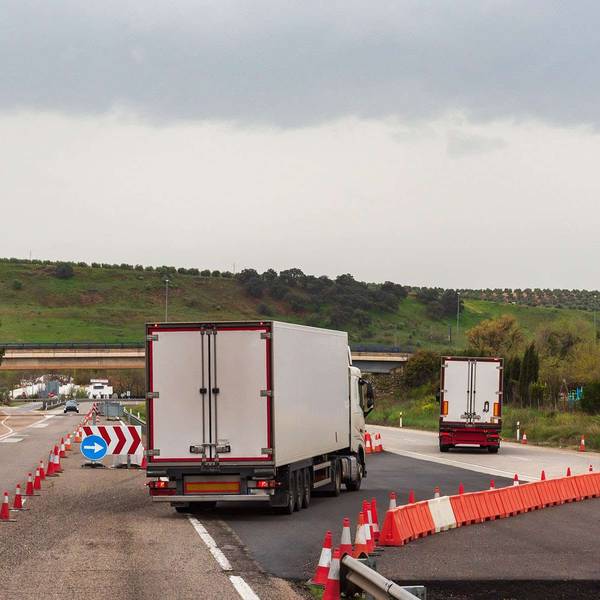 Two semi-trucks travel through a construction zone on a freeway.