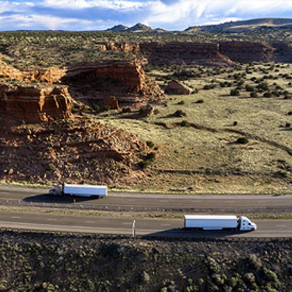 Two trucks on a winding road through a desert canyon landscape.
