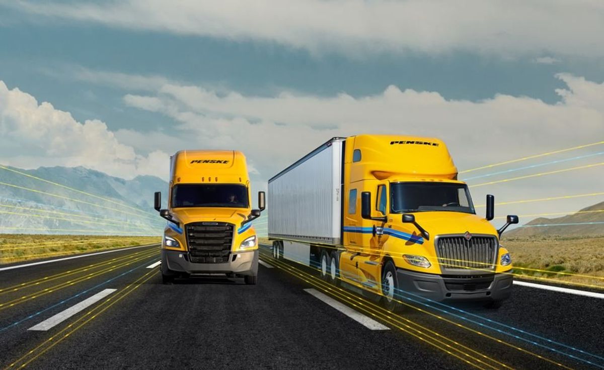 Two yellow Penske trucks driving down the highway