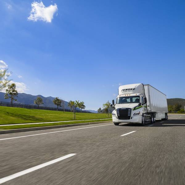 White electric Penske tractor-trailer drives on a sunny day.