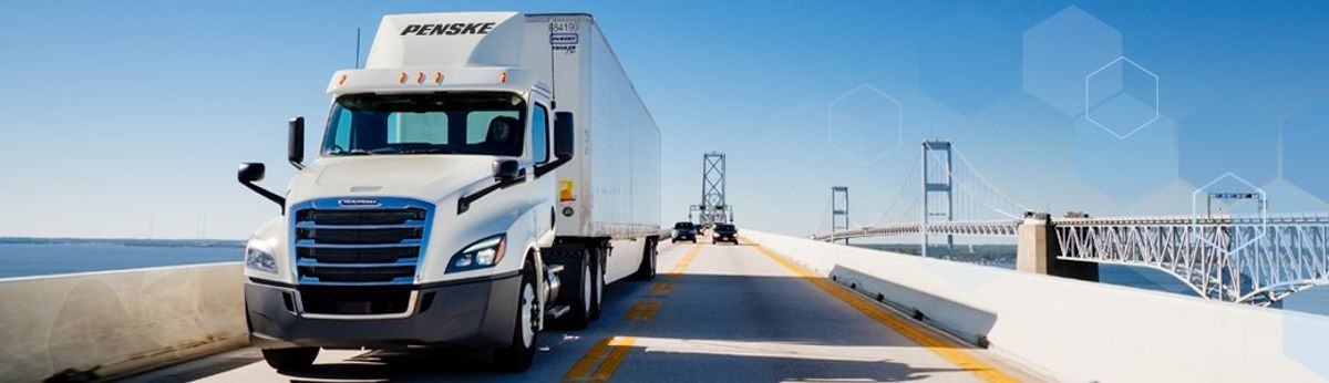 White Penske semi-truck drives over a bridge.