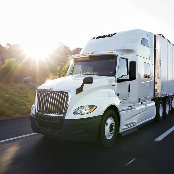 White Penske semi-truck driving on a freeway on a sunny day.