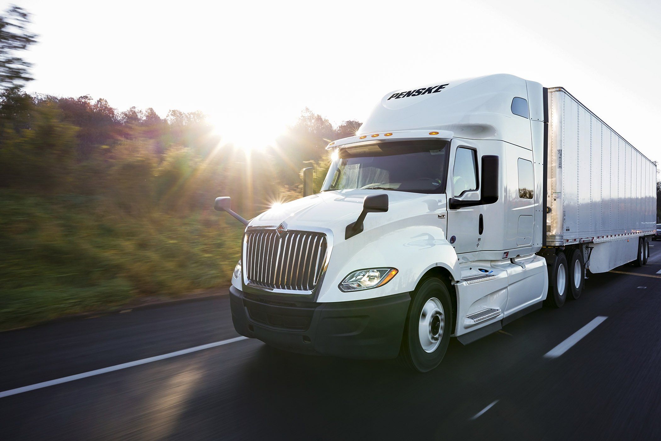 White Penske semi-truck driving on a freeway on a sunny day.