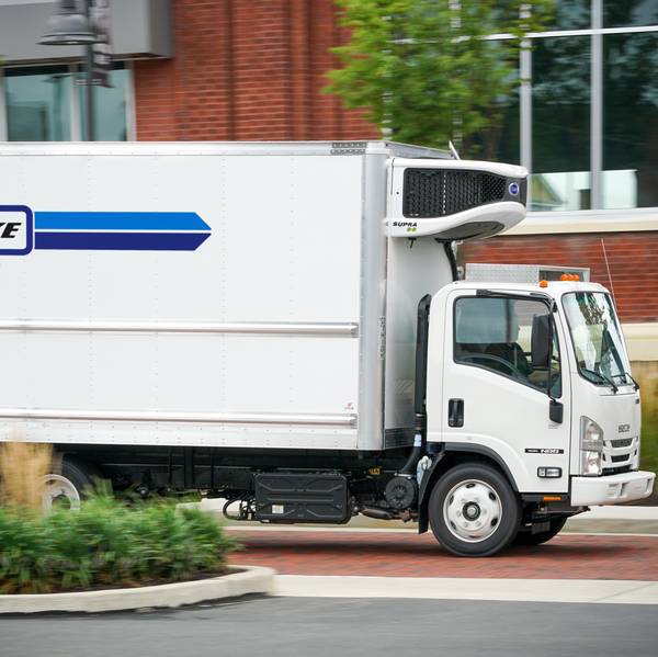 White refrigerated delivery truck driving past a brick building.