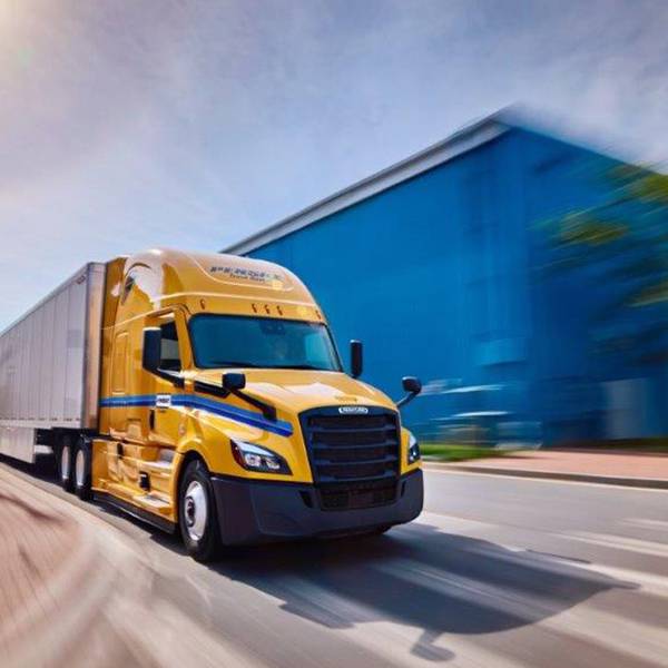 Yellow Penske tractor with trailer drives up a road.